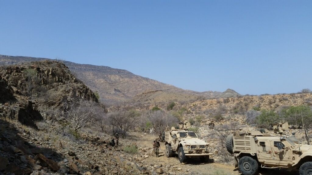 Heavy military vehicles and soldiers in a rugged desert landscape, showcasing durable tactical fabrics and textiles used in military and tactical equipment by Equites.
